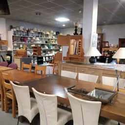 Winkelvloer met houten eettafels, stoelen en diverse meubels en huishoudartikelen op de achtergrond