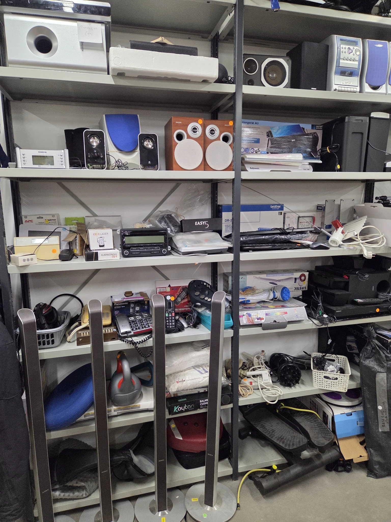 Metalen stellingen met elektronische apparaten, speakers, computers en huishoudelijke spullen