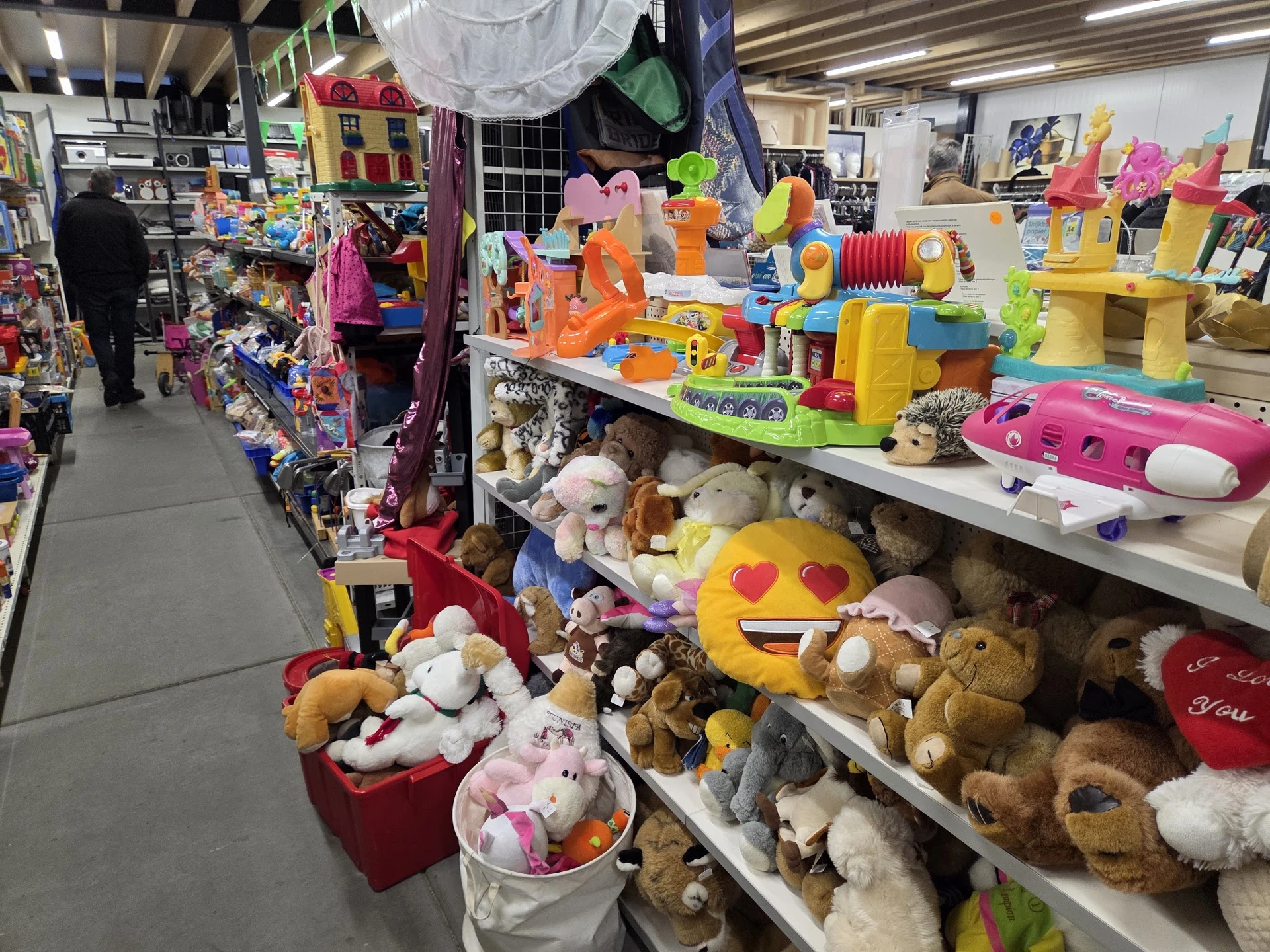 Uitgestalde speelgoed en knuffels op tafels en stellingen in de kringloopwinkel
