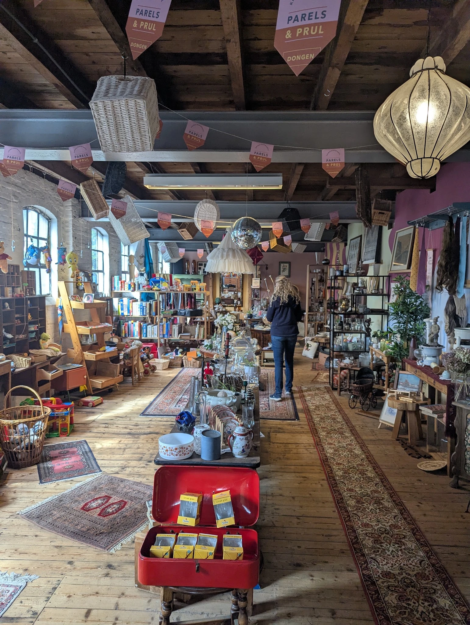 Ruim en gezellig interieur van kringloopwinkel met houten vloer, veel rekken met diverse tweedehands spullen, boeken, decorat