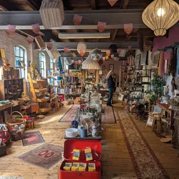 Ruim winkelbinnenaanzicht van kringloopwinkel met houten vloer, stellingen, hangende lampionnen en diverse tweedehands spulle