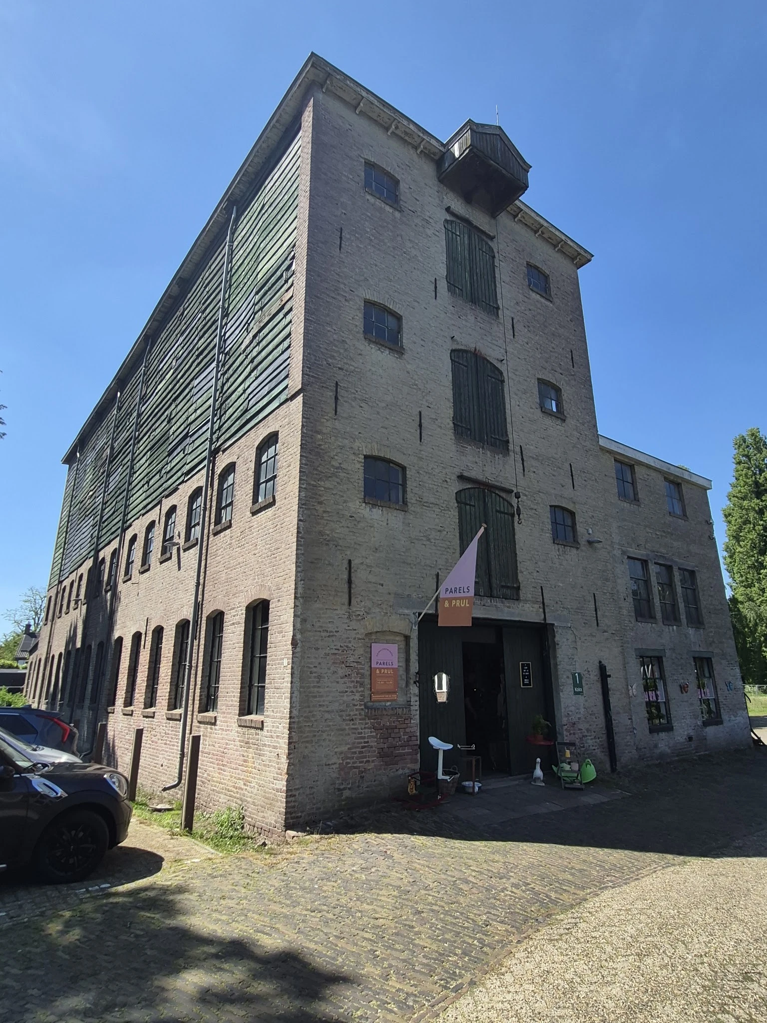 Bakstenen kringloopwinkel met meerdere verdiepingen en grote ramen aan hoek Heuvelstraat