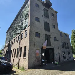 Bakstenen kringloopwinkel met meerdere verdiepingen en grote ramen aan hoek Heuvelstraat