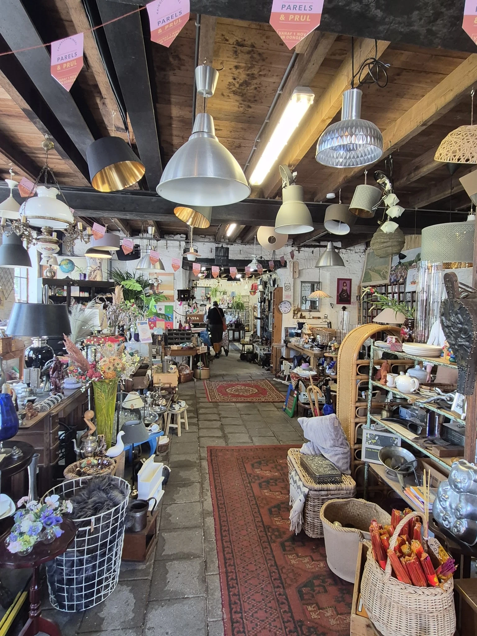 Binnenaanzicht van kringloopwinkel met lampen aan plafond, stellingen, planken met diverse gebruiksartikelen en decorstukken