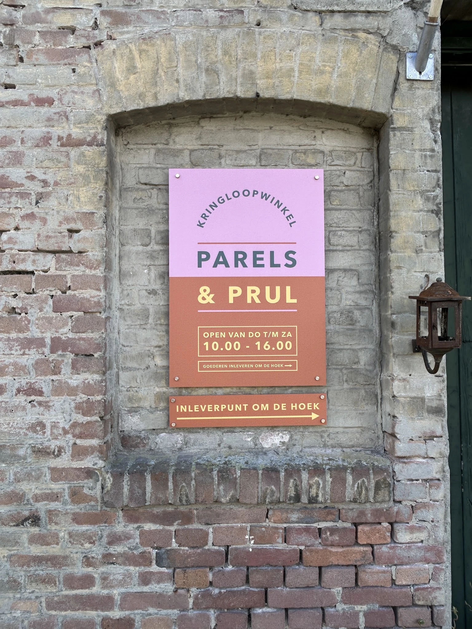 Roze en terracotta uithangbord aan bakstenen gevel met winkelname en openingstijden