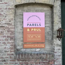Roze en terracotta uithangbord aan bakstenen gevel met winkelname en openingstijden