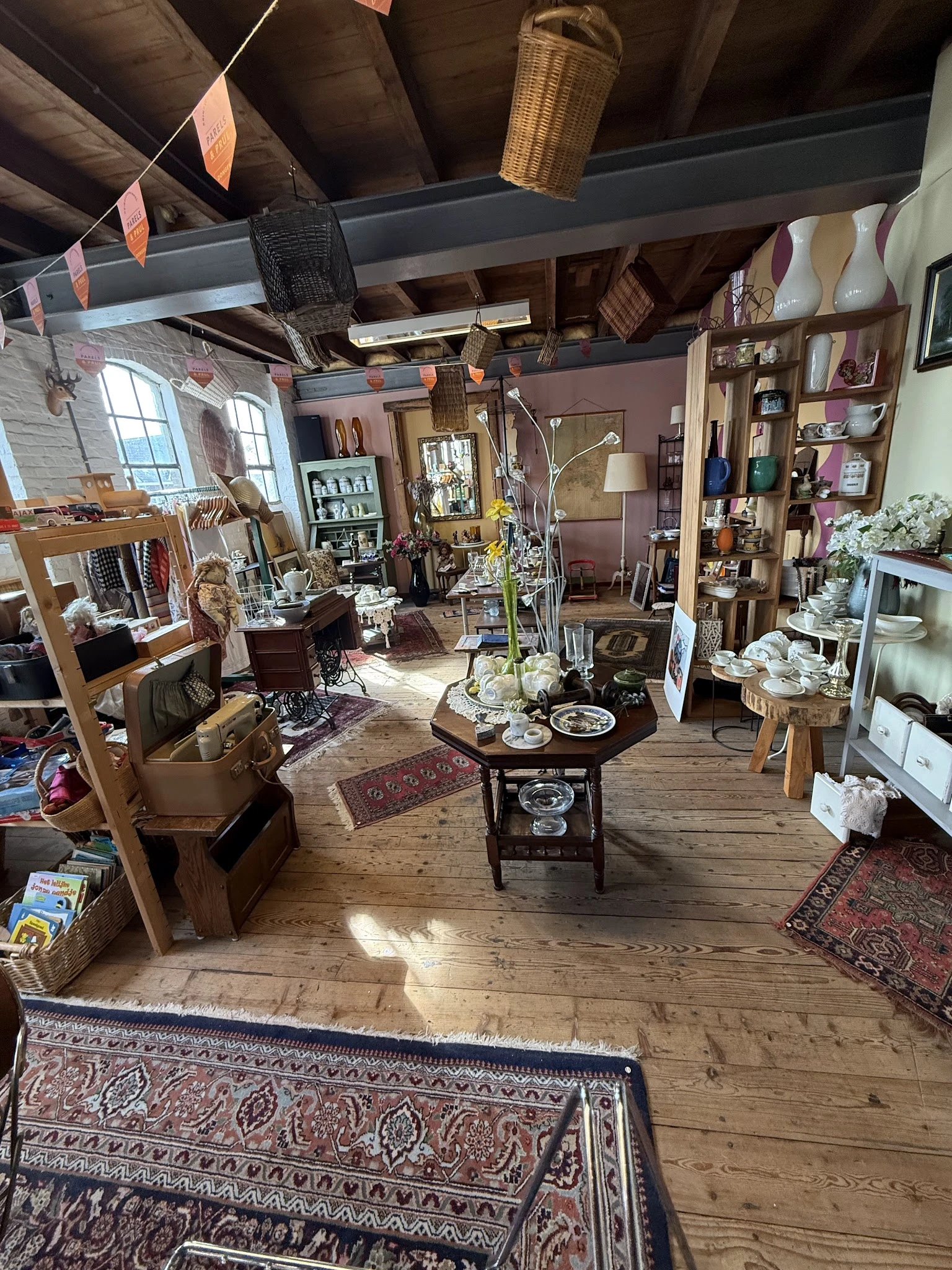 Overzicht van de winkelruimte met houten tafels, stellingen, decoratieve items en vintage meubels verspreid door de zaak