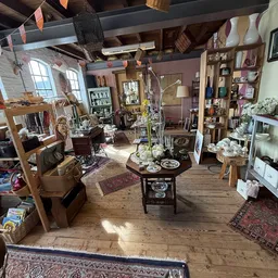 Overzicht van de winkelruimte met houten tafels, stellingen, decoratieve items en vintage meubels verspreid door de zaak