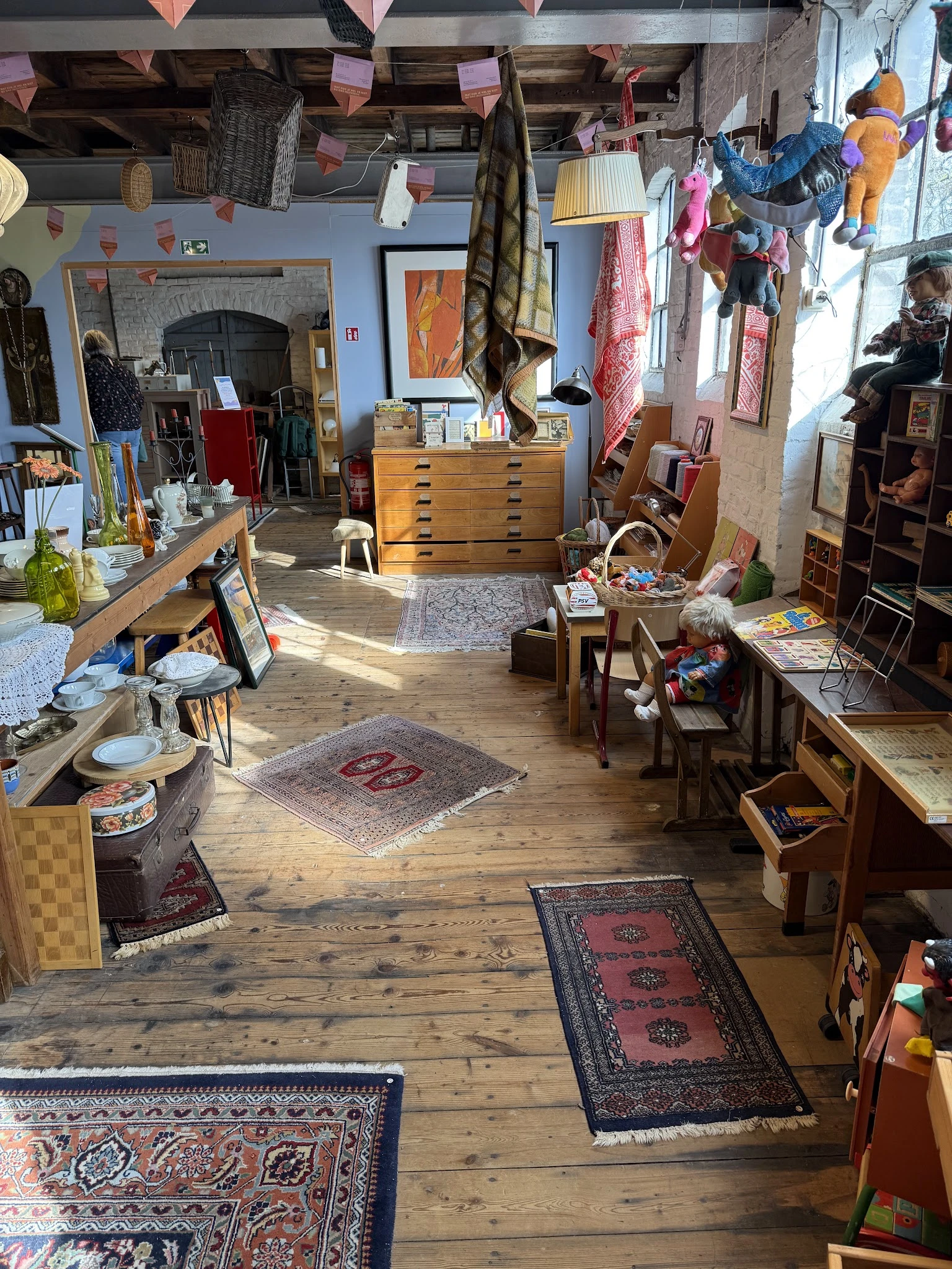 Overzicht van kringloopwinkelinterieur met houten vloer, diverse meubels, textiel en spullen verspreid door de ruimte