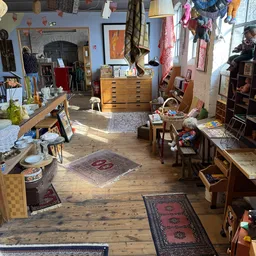 Overzicht van kringloopwinkelinterieur met houten vloer, diverse meubels, textiel en spullen verspreid door de ruimte