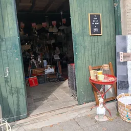 Ingang van kringloopwinkel met zicht op donker interieur vol spullen, rode stoelen en meubels buiten op straat