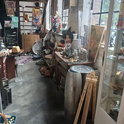 Kringloopwinkel met diverse gebruikte spullen: grote metalen kan, houten planken, schilderijen, lampen en ander huishoudelijk