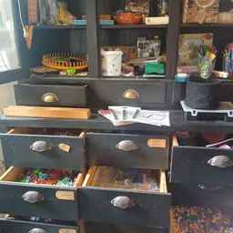 Donkergroene ladenkast met open laden vol gekleurde spullen en voorwerpen, met planken erboven met diverse items