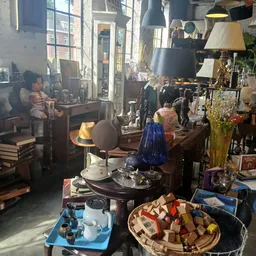 Interieur van kringloopwinkel met tafels vol spullen, lampen, kleding en diverse tweede-hands artikelen