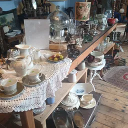 Uitgestalde serviesgoed, kannen, kopjes en schaaltjes op houten tafels met kant kleedje