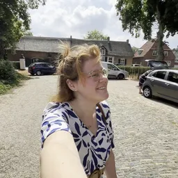 Vrouw met bril en gestreepte blouse op parkeerplaats met auto's en gebouwen