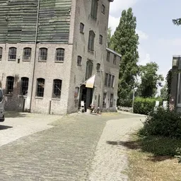 Bakstenen gebouw met grote ramen en klimop, binnenplein met kasseien