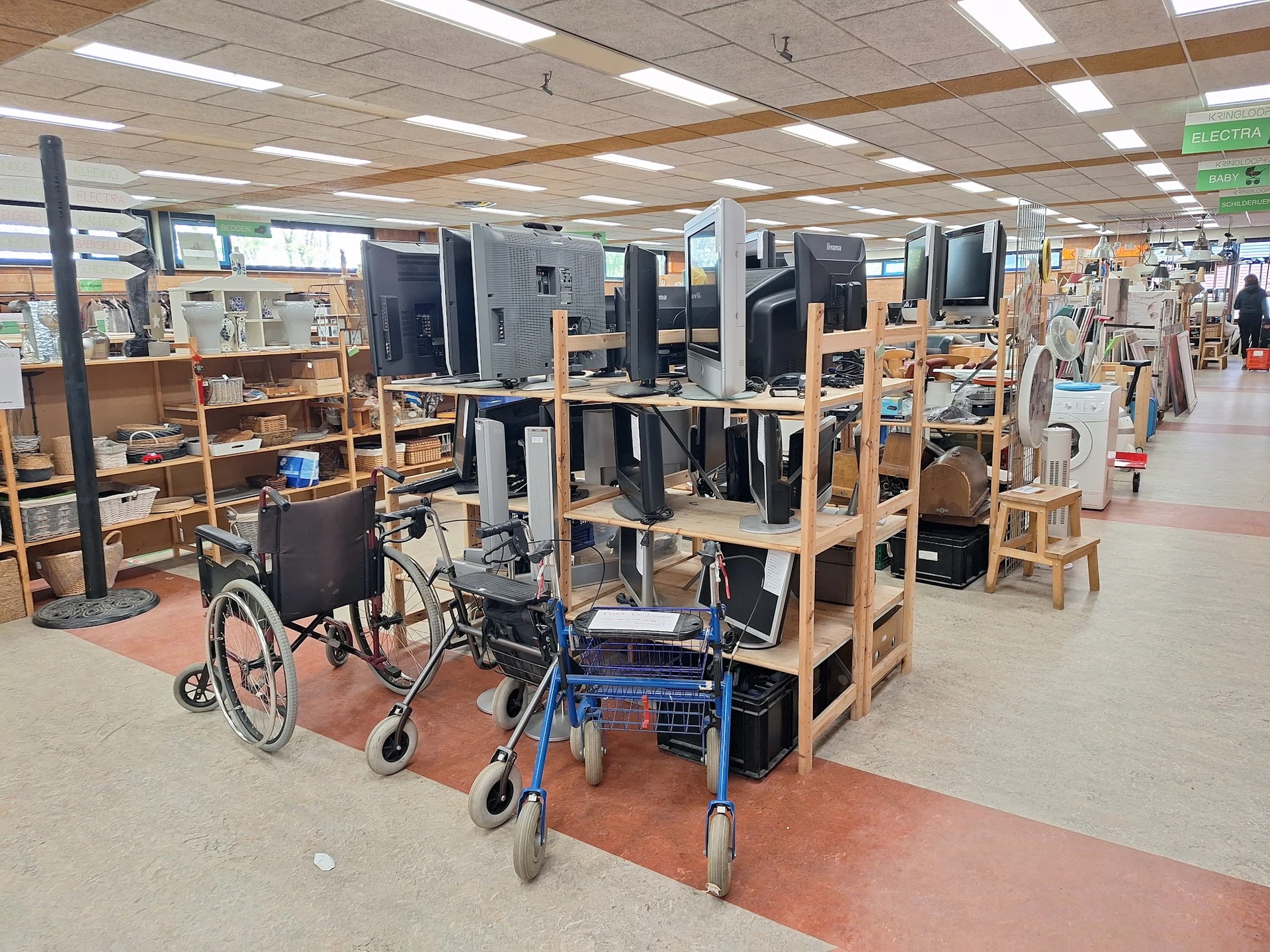 Winkelinterieur met houten stellingen, computers, rolstoelen en loopwagen op rode vloermatten onder fluorescerend licht