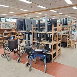 Winkelinterieur met houten stellingen, computers, rolstoelen en loopwagen op rode vloermatten onder fluorescerend licht