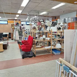 Winkelvloer van kringloopwinkel met stellingen vol spullen, rode fauteuil, kleding aan rekken en diversen huishoudartikelen