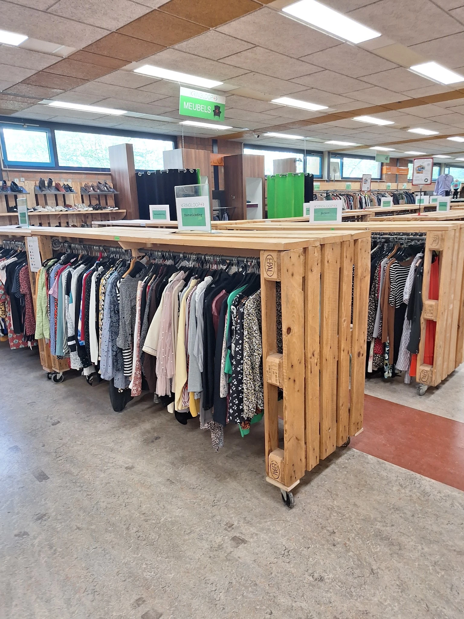 Houten kledingrekken met tweedehands kleding op hangers in verschillende kleuren en stijlen