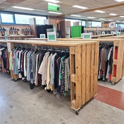 Houten kledingrekken met tweedehands kleding op hangers in verschillende kleuren en stijlen