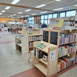 Winkelvloer met boekenkasten, stellingen met boeken en media, leestafel met gele blad, ramen met daglicht