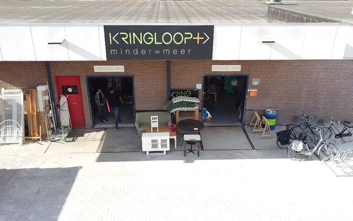 Gevel van Kringloop Plus met twee ingangsdeuren, uitstallingen en fietsen op het terras