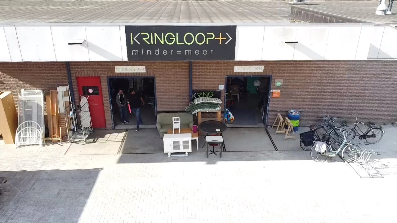 Gevel van Kringloop Plus met twee ingangsdeuren, uitstallingen en fietsen op het terras