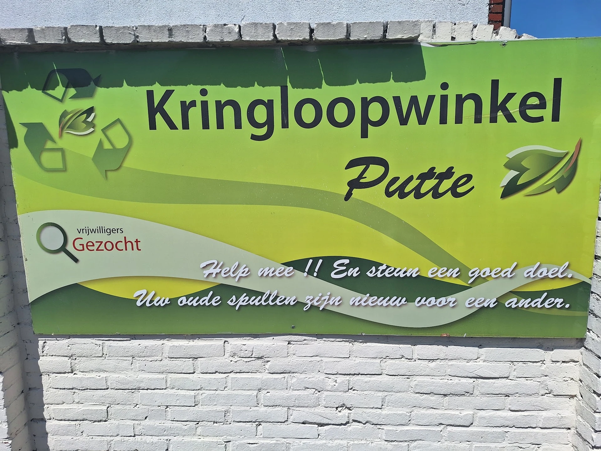 Groene gevel met Kringloopwinkel Putte-logo en Gezocht-label op witte bakstenen muur