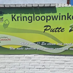 Groene gevel met Kringloopwinkel Putte-logo en Gezocht-label op witte bakstenen muur