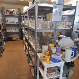 Gangpad in kringloopwinkel met stellingen vol huishoudartikelen, servies en keukengerei