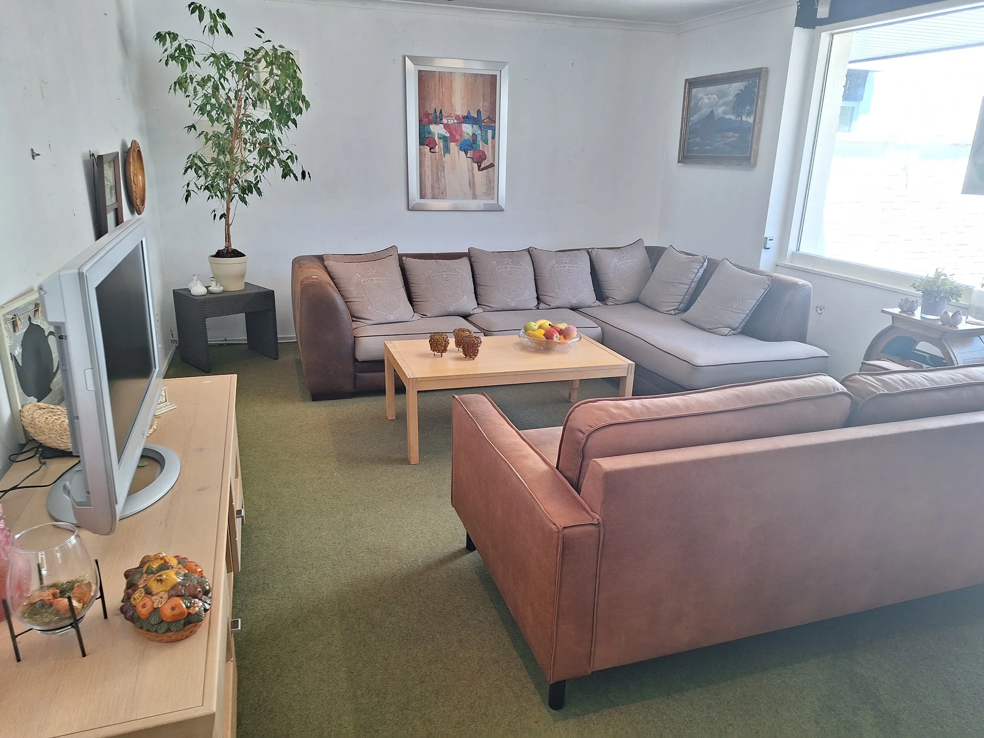 Woonkamer inrichting met grijze hoekbank, roze fauteuil en houten salontafel