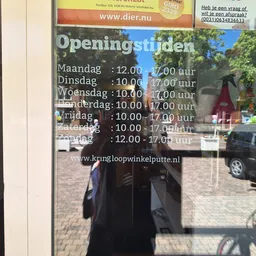 Openingstijden van een winkel weergegeven op een raam, met wagen en parkeerplaats zichtbaar achter het glas