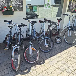 Rij van verschillende tweedehands fietsen en e-bikes buiten tegen een witte muur