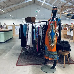 Kledingrek met tweedehands dameskleding en een etalagepop met oranje en blauwe jurk in kringloopwinkel