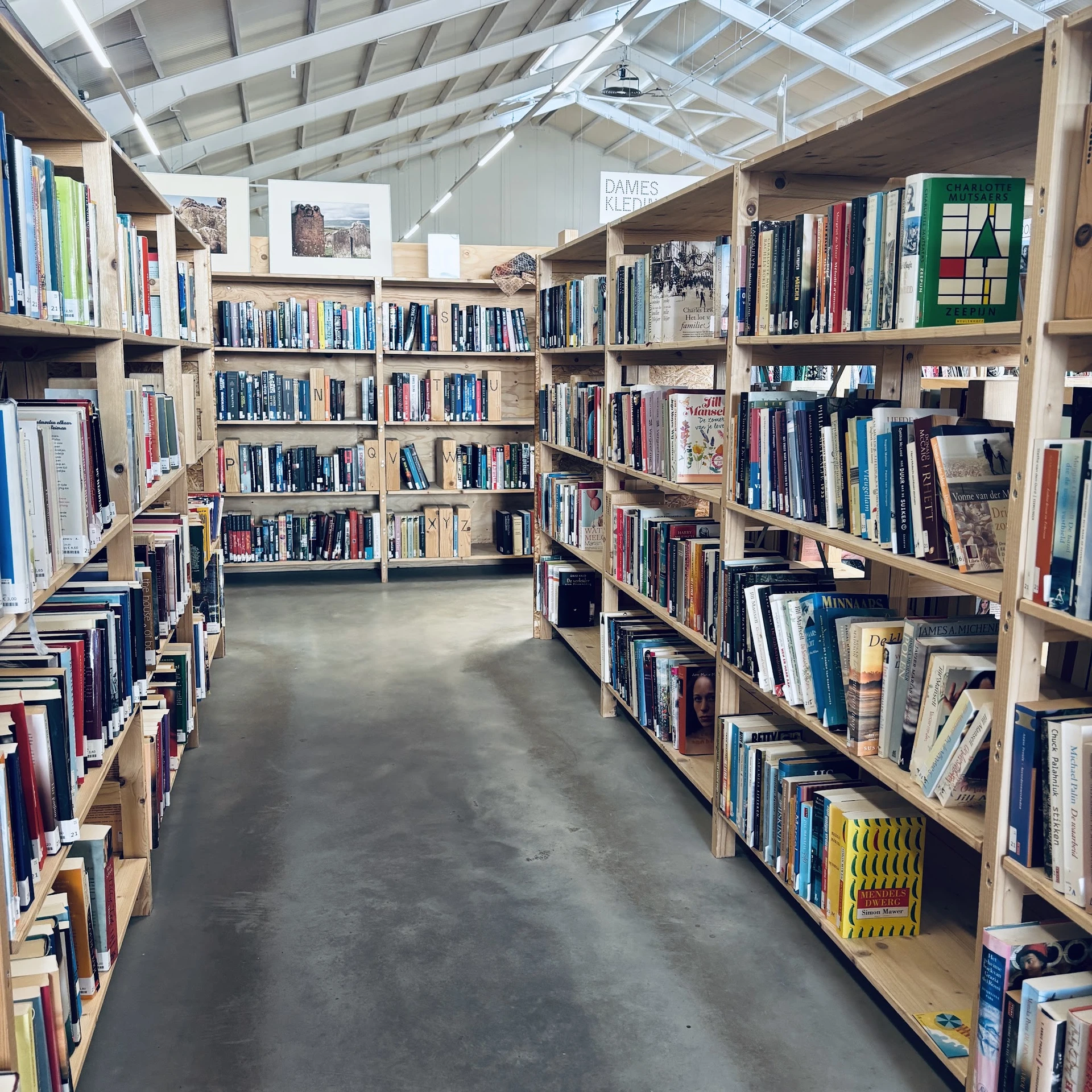 Boekenrekken met tweedehands boeken in een helderuit kringloopwinkel, zicht op stellingen langs het gangpad
