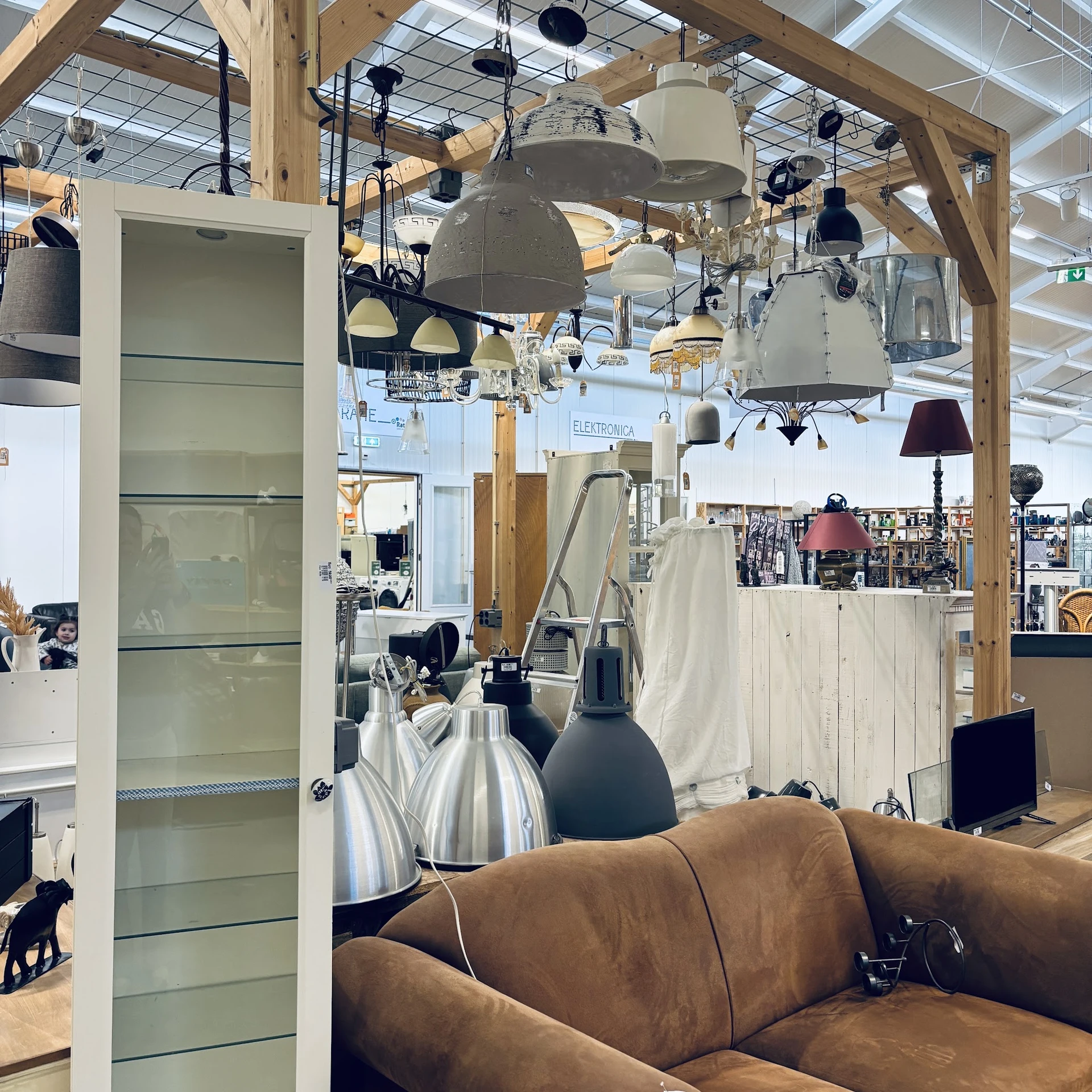 Winkelvloer met hanglampen, stellingen, een bruine bank en diverse artikelen in een kringloopwinkel