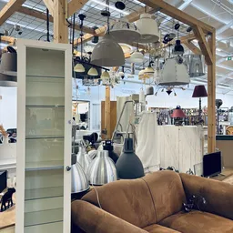 Winkelvloer met hanglampen, stellingen, een bruine bank en diverse artikelen in een kringloopwinkel