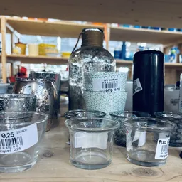 Glazen potjes en flessen met prijsstickers op een toonbank in een kringloopwinkel