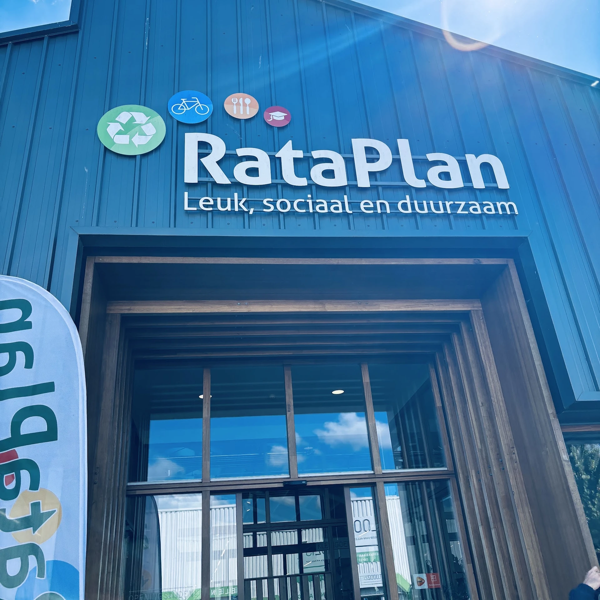 Gevel van kringloopwinkel RataPlan met blauwe gevelsteen, winkelnaam en logo's, entree met raam