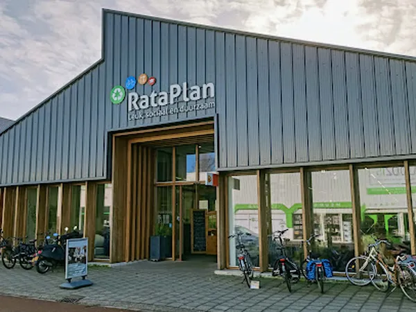 Moderne gevel van RataPlan kringloopwinkel met groene en houten accenten, ingang met grote ramen en fietsen geparkeerd ervoor