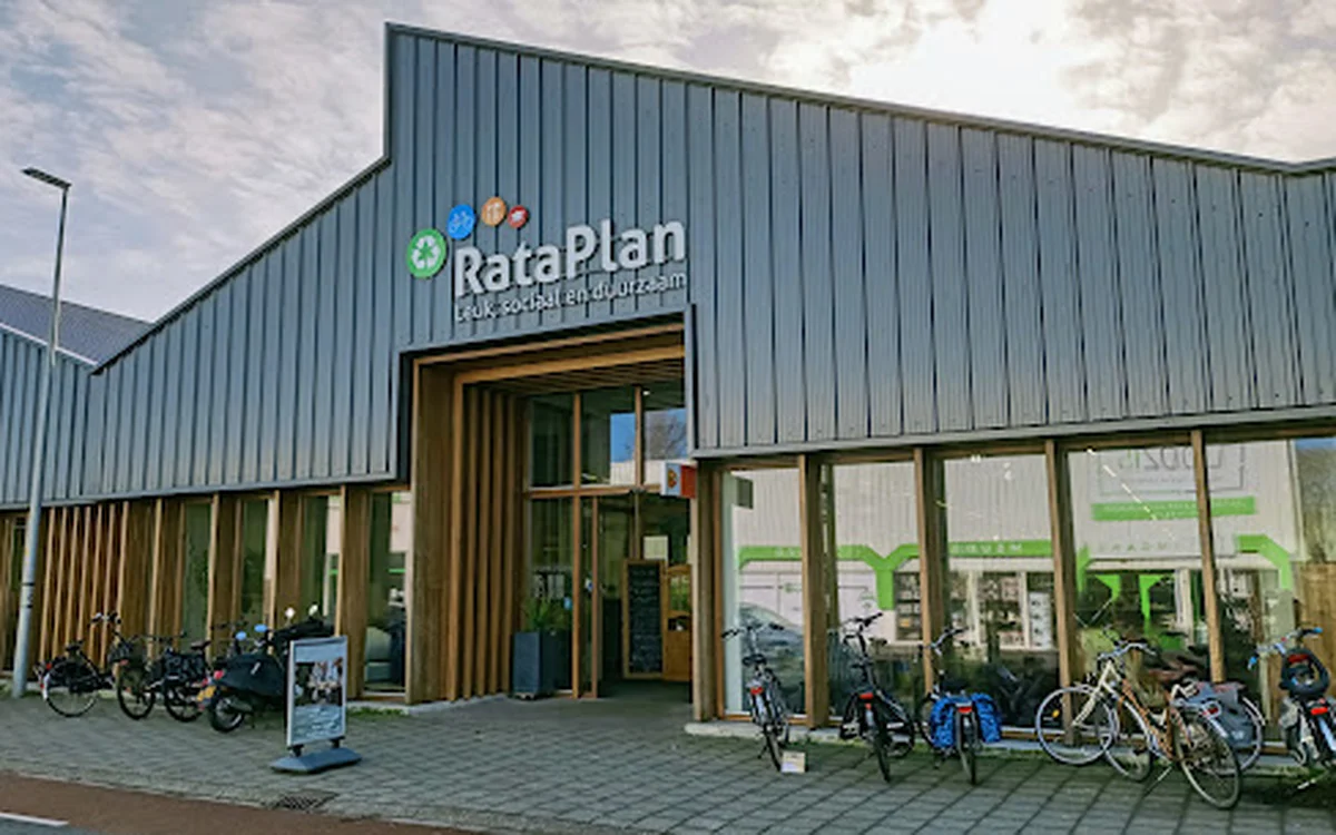 Moderne gevel van RataPlan kringloopwinkel met groene en houten accenten, ingang met grote ramen en fietsen geparkeerd ervoor