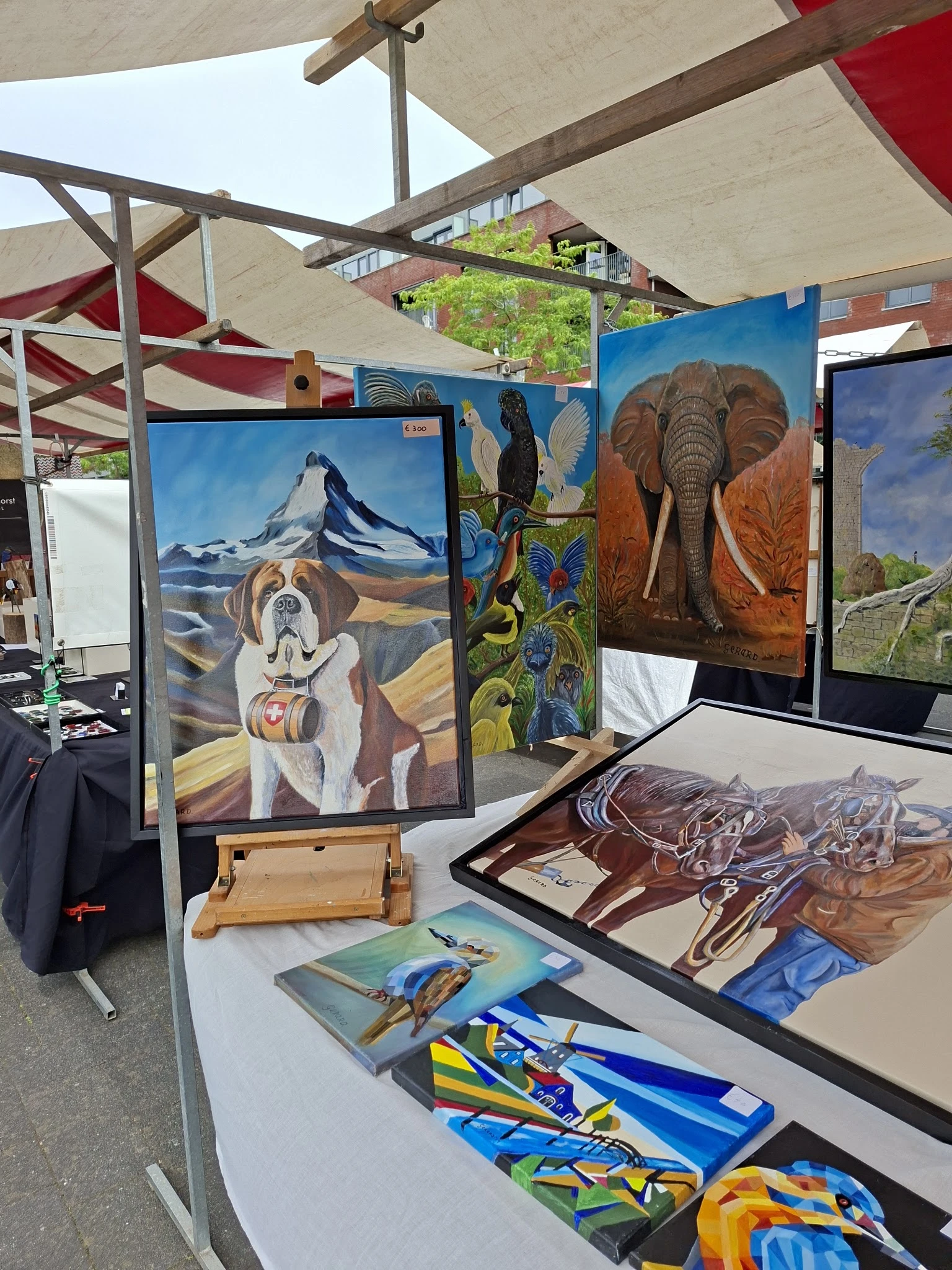 Kunstwerken en schilderijen op ezel en tegen wand in kringloopwinkel, waaronder hondenportret en olifantschilderij