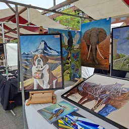 Kunstwerken en schilderijen op ezel en tegen wand in kringloopwinkel, waaronder hondenportret en olifantschilderij