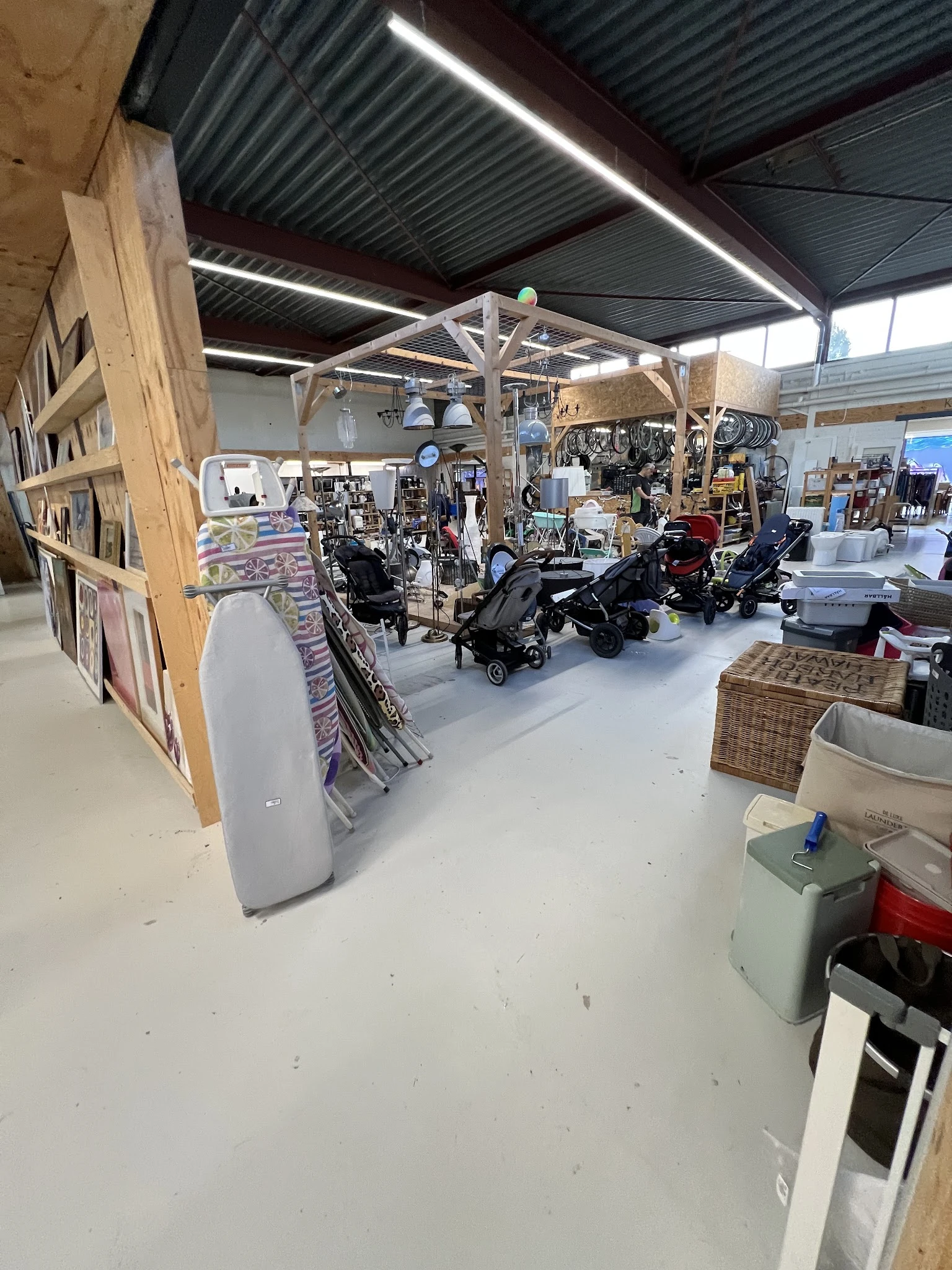 Overzicht van de winkelvloer met kinderwagens, fietsen en diversen huishoudelijke spullen onder een houten constructie.