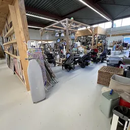 Overzicht van de winkelvloer met kinderwagens, fietsen en diversen huishoudelijke spullen onder een houten constructie.