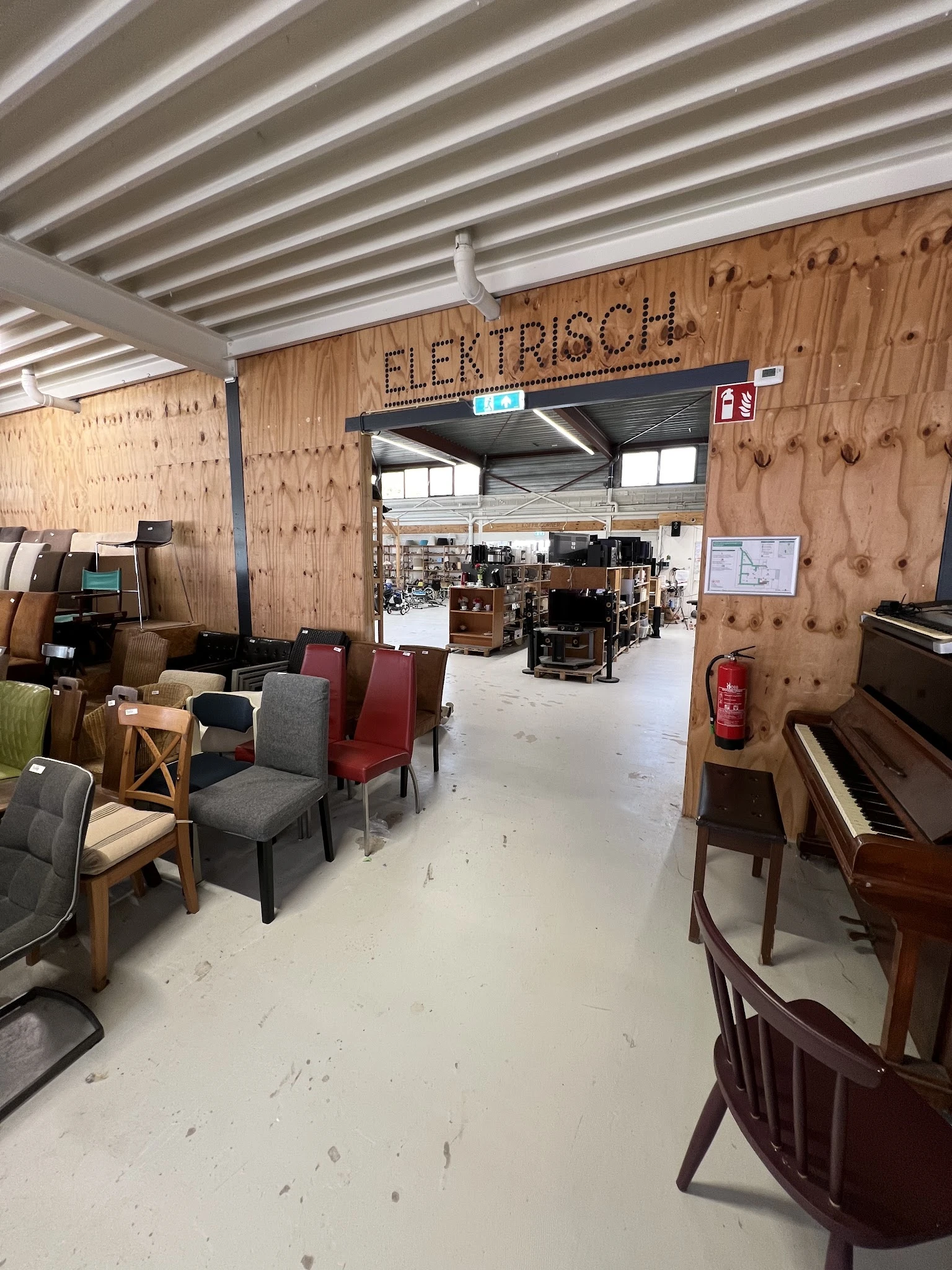 Winkelvloer met uitgestalde meubels, stoelen en een piano in een kringloopwinkel met houten wanden