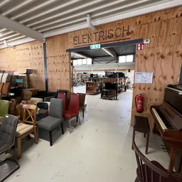 Winkelvloer met uitgestalde meubels, stoelen en een piano in een kringloopwinkel met houten wanden