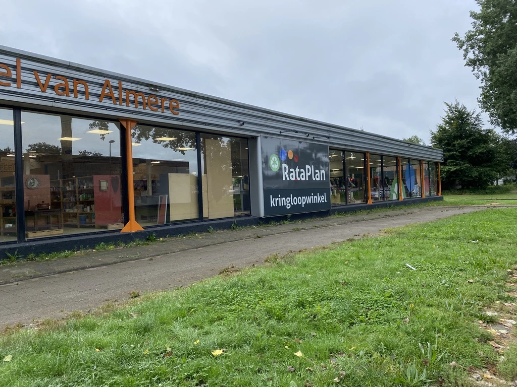 Voorgevel van kringloopwinkel met donkerblauwe pui, grote ramen en winkelnaam RataPlan zichtbaar